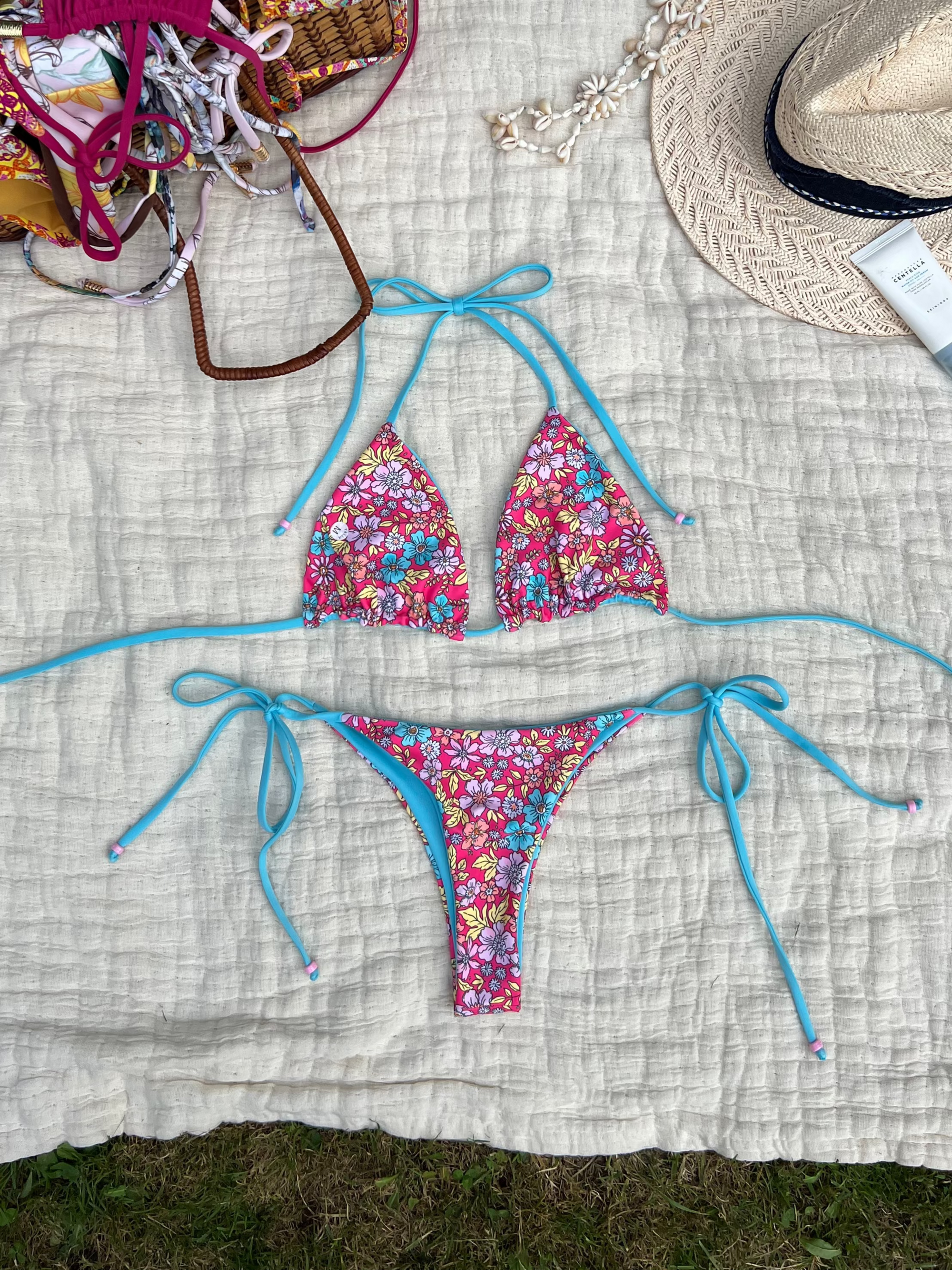 Colorful floral bikini set on a textured blanket with a hat and basket in the background.