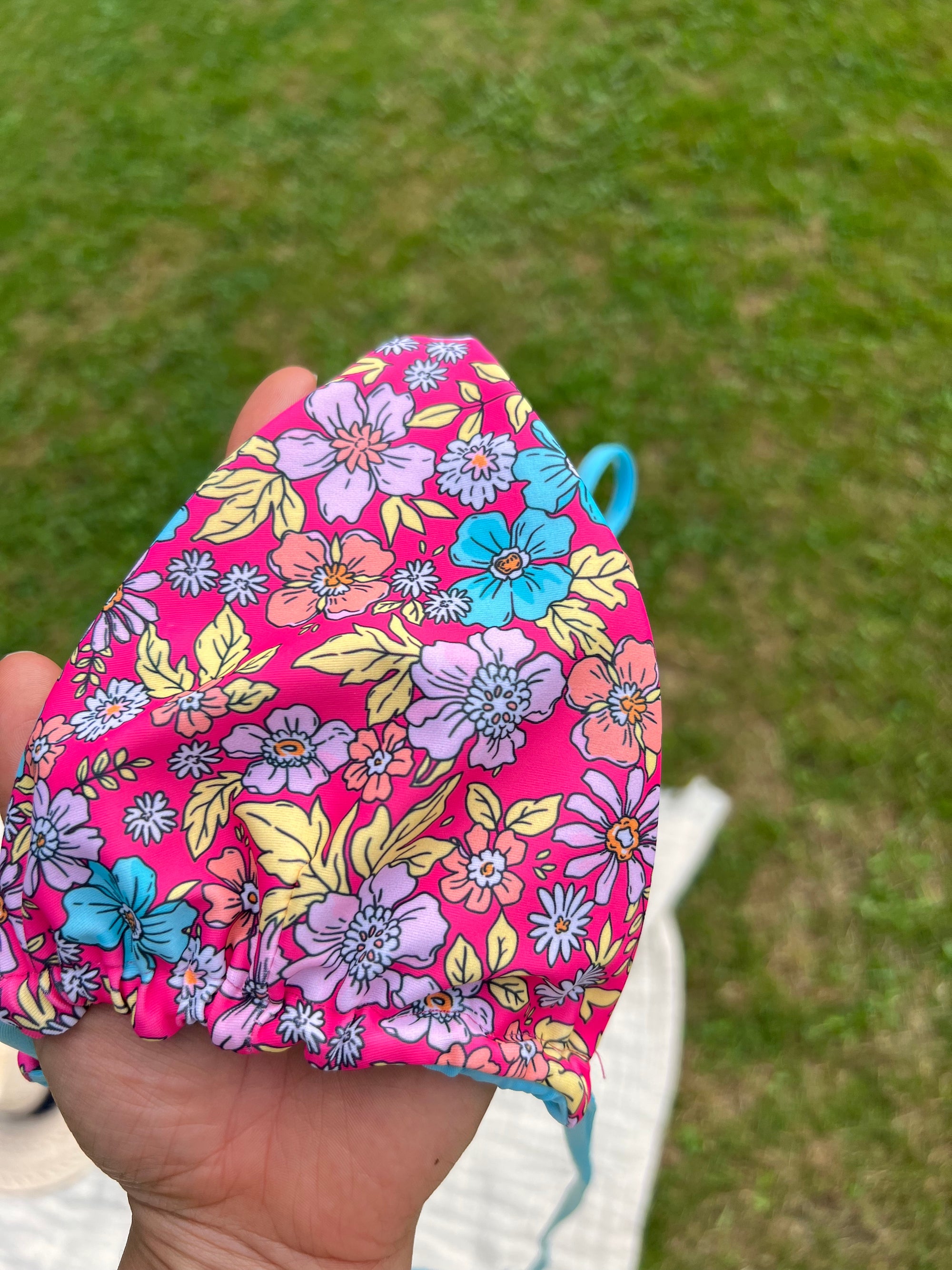 Floral-patterned pink bikini held by a hand with a grassy background