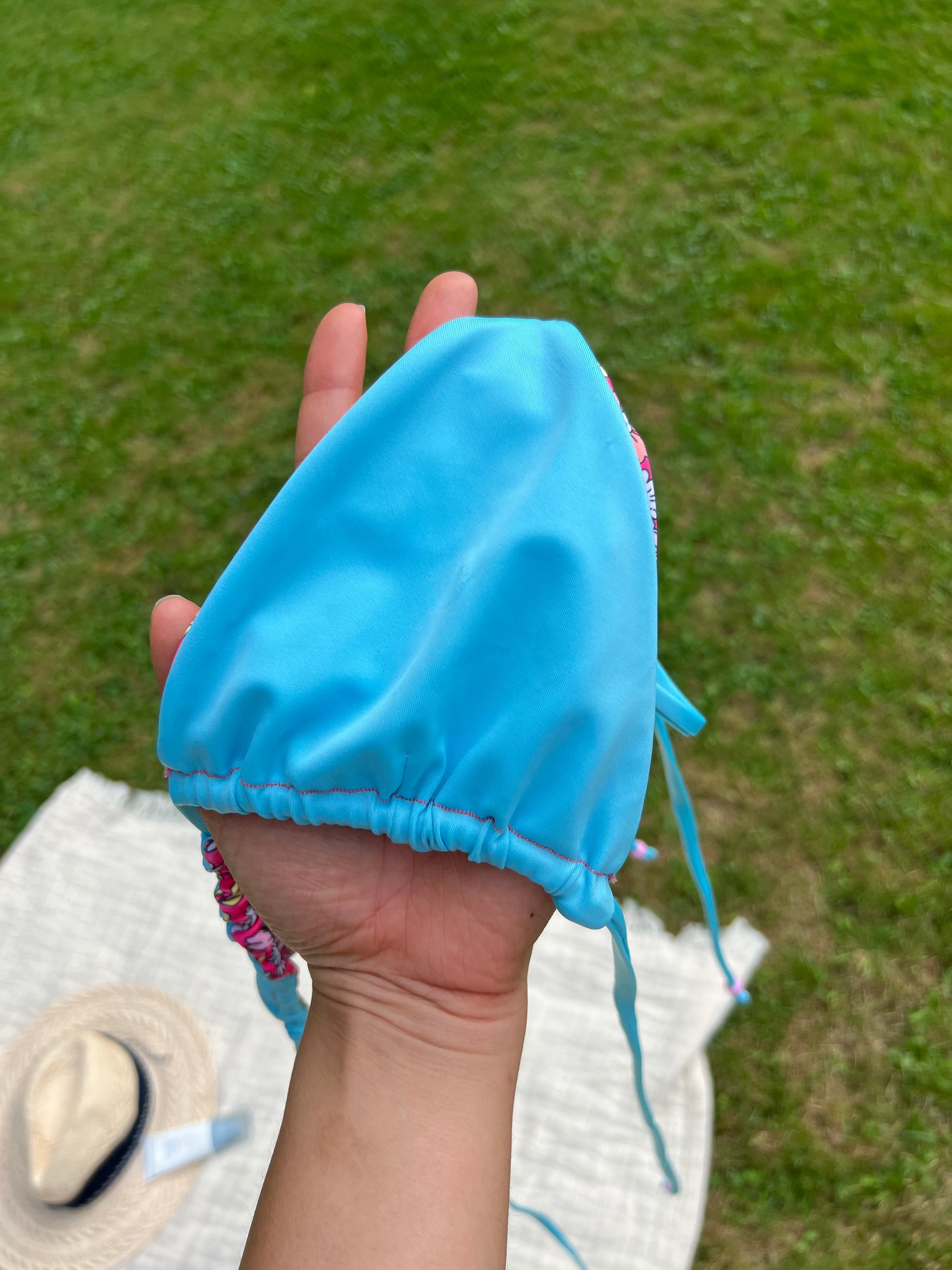 Hand holding a blue bikini top against a grassy background