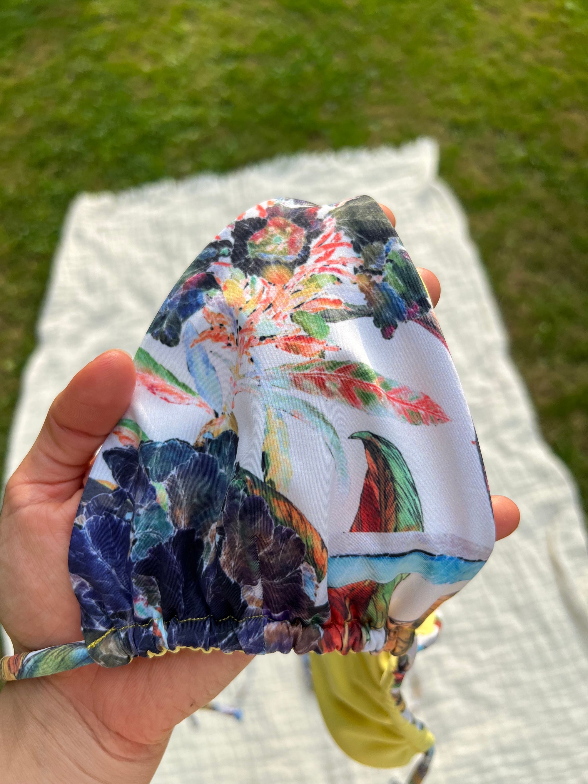 Colorful floral-patterned bikini top held by a hand with a grassy background